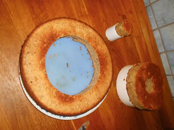 Eine dreistöckige Nusstorte auf einem Holztablett, mit einer blauen Füllung und einem kleinen Kuchen daneben, wartet auf Dekoration.