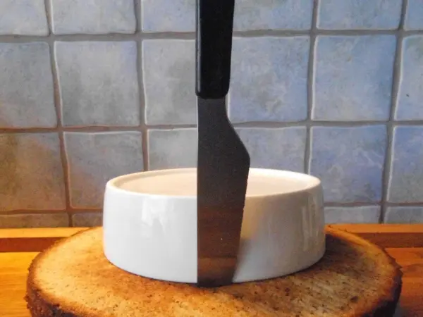 Eine dreistöckige Nusstorte steht auf einem Holzbrett, während ein großes Messer daneben eingeklemmt ist, bereit zum Schneiden.