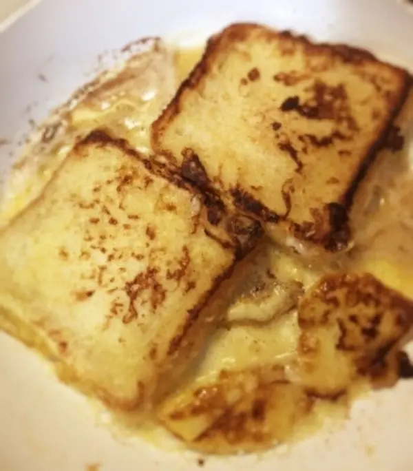 Drei goldbraun gebratene French Toast-Scheiben liegen in einer weißen Schüssel, umgeben von leicht süßem Ahornsirup.