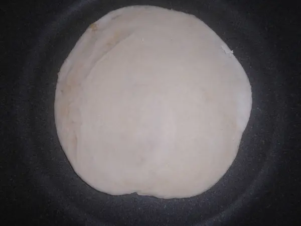 Ein runder Teigkreis liegt in einer heißen Bratpfanne und wird goldbraun gebacken für das Pfannenbrot.