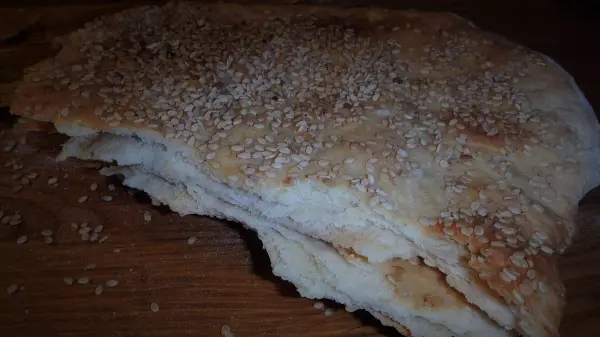 Ein Fladenbrot liegt auf einem Holzbrett, leicht knusprig und mit Sesampaste bestreut, bereit zum Servieren.