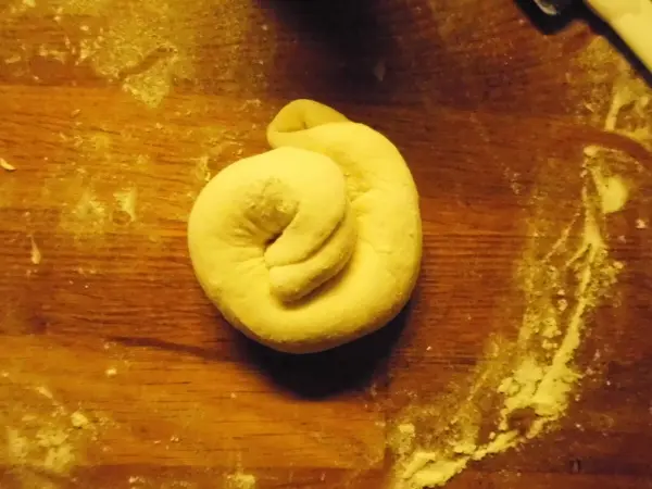 Ein Teigstück zieht sich spiralig zusammen und liegt auf einer bemehlten Arbeitsfläche, bereit zum weiteren Verarbeiten.