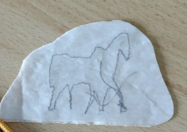 Ein transparenter Vlieseline-Ausschnitt zeigt eine Pferdesilhouette, während er auf eine Holzoberfläche gelegt wird.