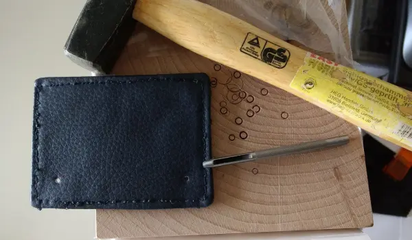 Ein schwarzes Griffpolster liegt auf einem Holzbrett, während ein Hammer daneben liegt, bereit zum Nähen und Basteln.