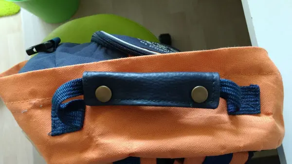 Ein Rucksack mit einem orangefarbenen Griffpolster, das stabil angenäht ist, liegt auf einem Tisch in einem hellen Raum.