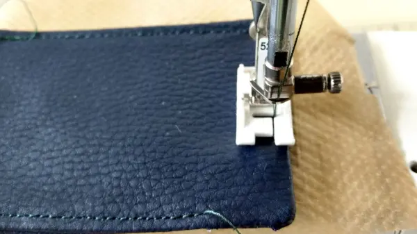 Ein Nähfuß näht ein dunkelblaues Griffpolster aus Leder, während sich der Stoff auf einer Nähmaschine befindet.