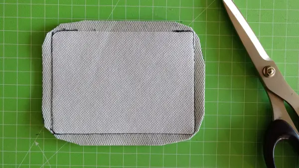 Ein graues Griffpolster für einen Rucksack liegt auf einem grünen Schneidemattenhintergrund neben einer Schere.