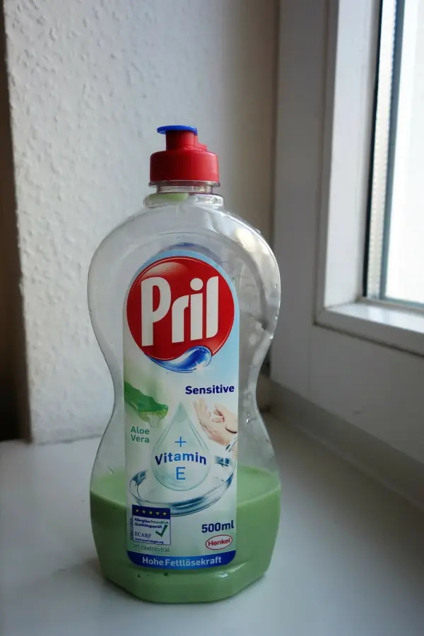 Eine grüne Spülmittelflasche von Pril steht auf einer Fensterbank. Text: "Sensitive, Aloe Vera, Vitamin E, 500 ml, Hohe Fettlösekraft."