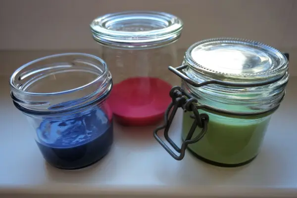 Drei Gläser enthalten selbstgemachte Kinderfarbe in Blau, Rot und Grün und stehen auf einer weißen Oberfläche.