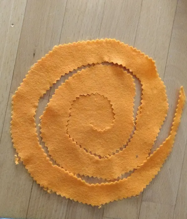 Ein orangefarbener Filzstreifen ist spiralförmig ausgelegt, um dekorativ für einen Osterkranz verwendet zu werden.