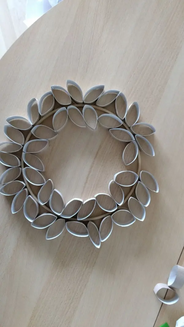 Ein dekorativer Osterkranz aus Papierrollen liegt auf einem Holztisch und wartet darauf, mit Leckereien geschmückt zu werden.