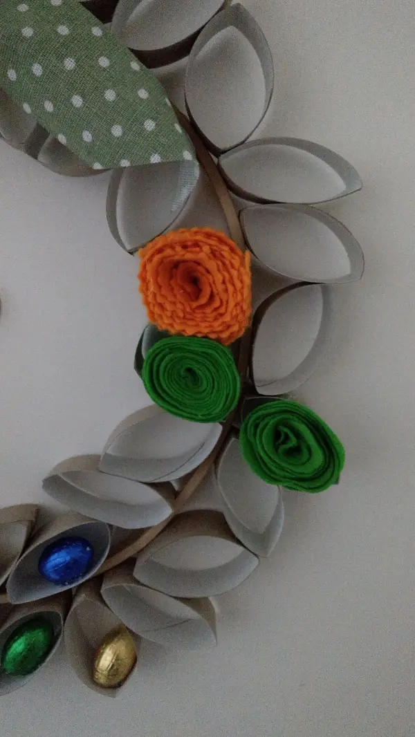 Ein Osterkranz aus Papprollen mit bunten Blumen und Schokoladeneiern dekoriert, präsentiert festlichen Frühlingszauber.