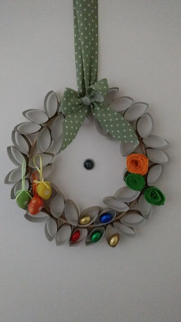 Ein dekorativer Osterkranz mit bunten Eiern und Blumen hängt an einer Wand, um festliche Stimmung zu verbreiten.