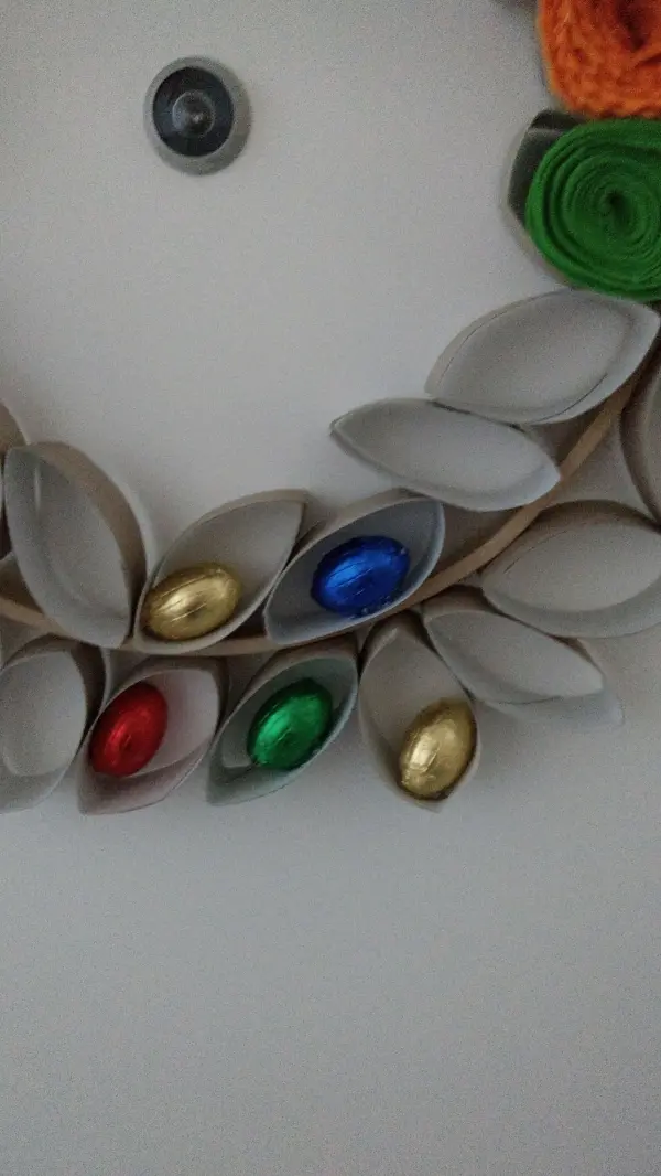 Ein bunter Osterkranz aus Papier, dekoriert mit bunten Eiern, hängt an der Wand und lädt zum Naschen ein.