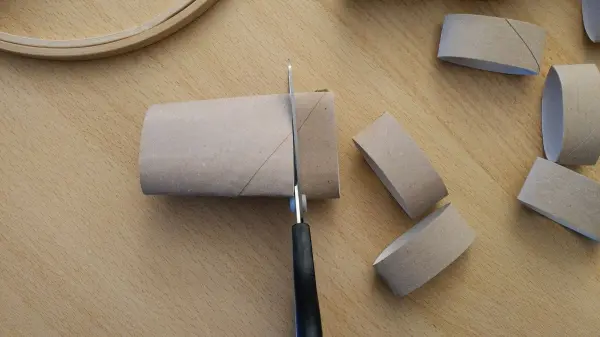 Ein Papprollenteil wird mit einer Schere in kleinere Stücke geschnitten, um einen kreativen Osterkranz zu gestalten.