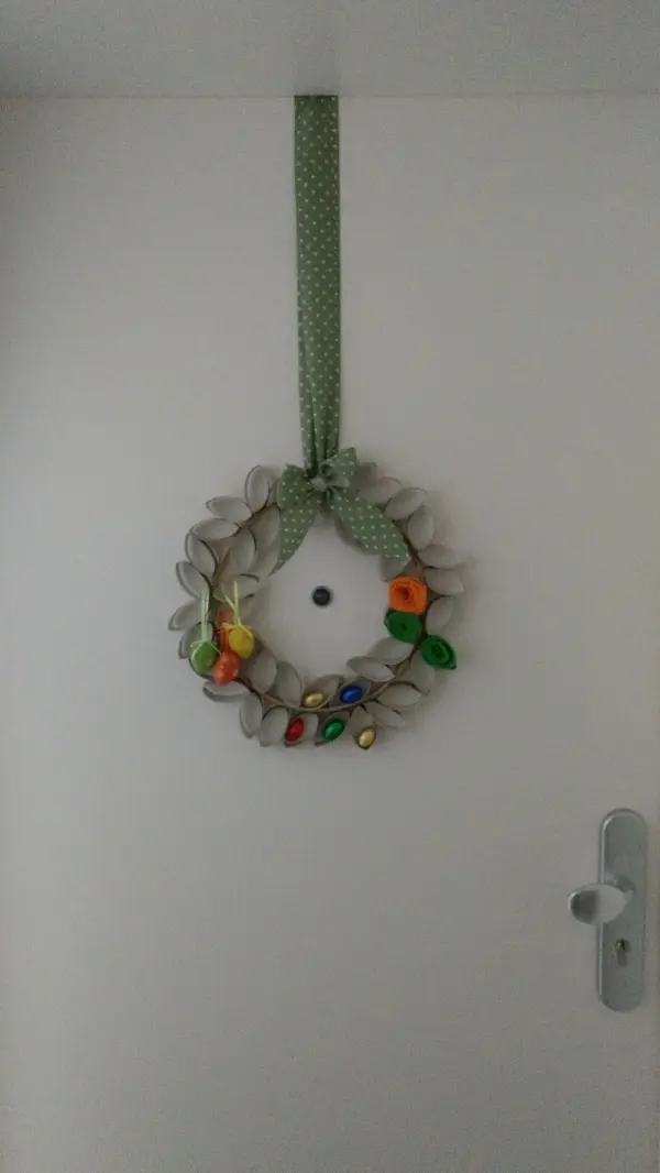Ein dekorativer Osterkranz hängt an einer Tür, geschmückt mit bunten Eiern und einer grünen Schleife, lädt zum Naschen ein.