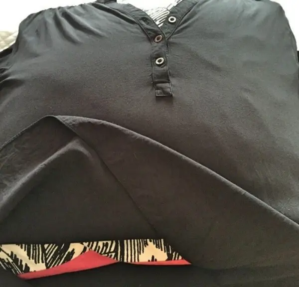 Ein schwarzes T-Shirt liegt ordentlich gefaltet auf einer Fläche, bereit zum Glätten ohne Bügeleisen in einem wohnlichen Umfeld.