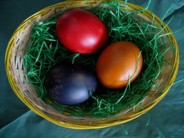Ein Korb enthält kräftig gefärbte Ostereier in Rot, Schwarz und Braun, umgeben von grünem Stroh.