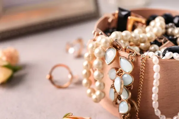 Eine Schmuckschatulle mit Vintage-Schmuck und Perlen liegt auf einem Tisch, umgeben von soften Blumen und einem Spiegel.
