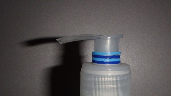 Ein Seifenspender gibt Flüssigkeit ab, vor grau-schwarzem Hintergrund, Schattenspiel zur linken Seite.