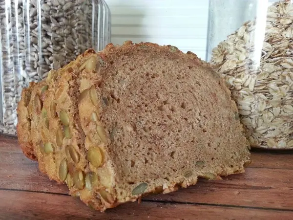 Ein Laib Dinkelbrot steht auf einem Tisch, umgeben von Glasbehältern mit Getreide. Es wirkt frisch und einladend.