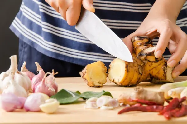 Hände schneiden frischen Ingwer und Knoblauch auf einem Holzbrett, um Gerüche zu entfernen und natürliche Hausmittel zu verwenden.