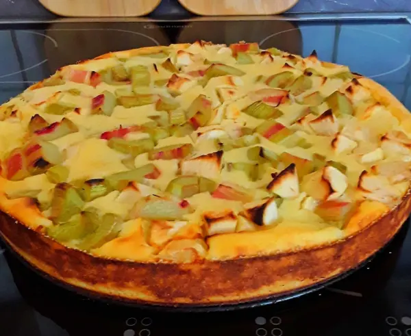 Ein Käsekuchen ohne Boden mit Rhabarberstücken ist frisch aus dem Ofen. Er steht auf einer Arbeitsfläche in einer modernen Küche.