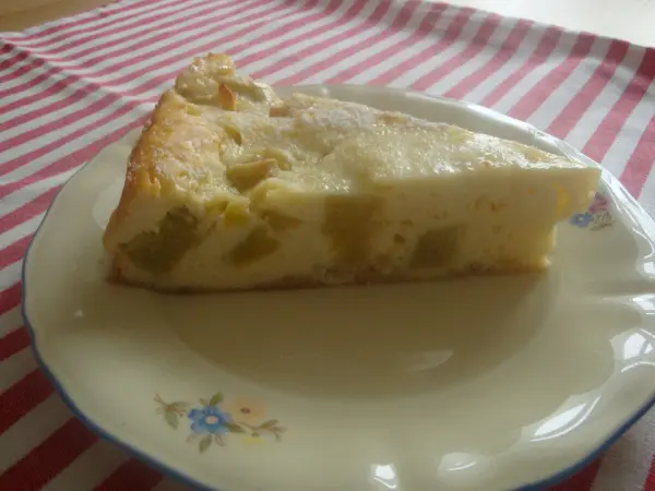 Ein Stück Rhabarber Käsekuchen ohne Boden liegt auf einem dekorativen Teller, umgeben von einem gestreiften Tuch.