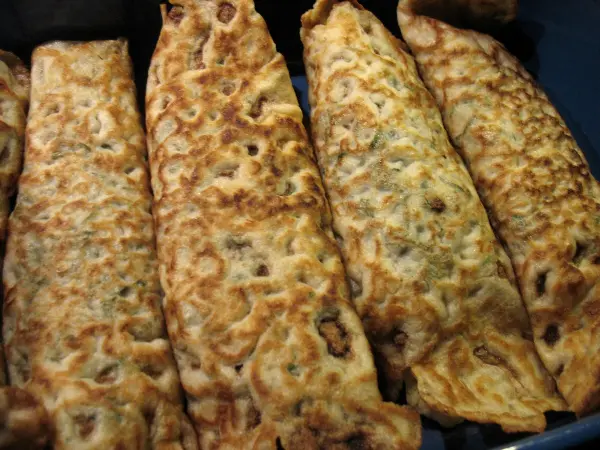 Überbackene Crepes mit einer goldbraunen, knusprigen Oberfläche liegen nebeneinander in einer Backform.