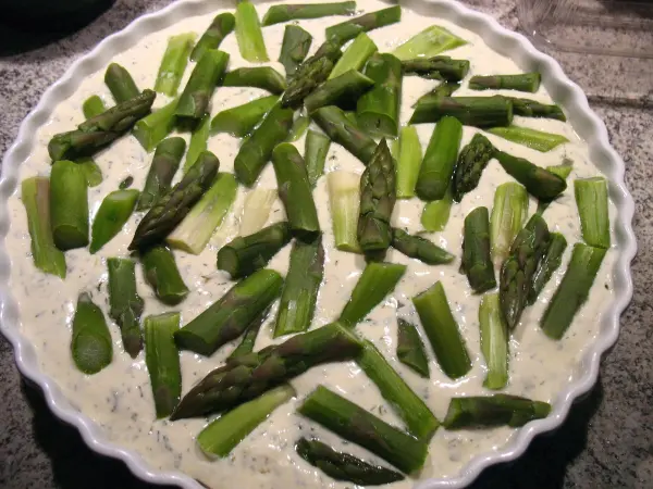 Eine Tarte mit frischem Spargel liegt auf der Arbeitsfläche, belegt mit grünem Spargel, bereit für das Backen.