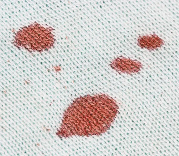 Rote Blutflecken sind auf einem hellen Stoff sichtbar, die auf eine Verschmutzung hindeuten und gereinigt werden müssen.