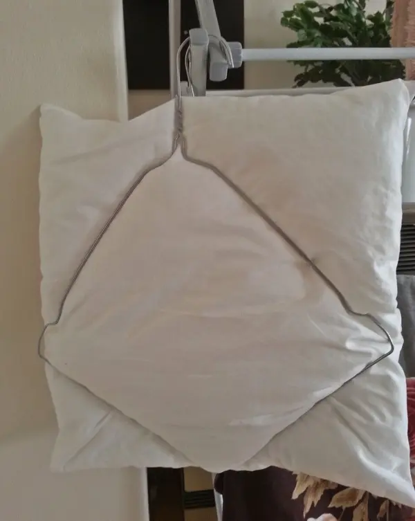Ein Drahtkleiderbügel hält ein gefaltetes Kissen zum Trocknen in einem Wohnraum, um Platz zu sparen.