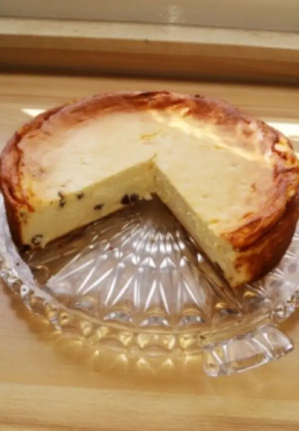 Ein Käsekuchen ohne Boden wird auf einem gläsernen Teller präsentiert. Ein Stück fehlt, was ihn appetitlich macht.