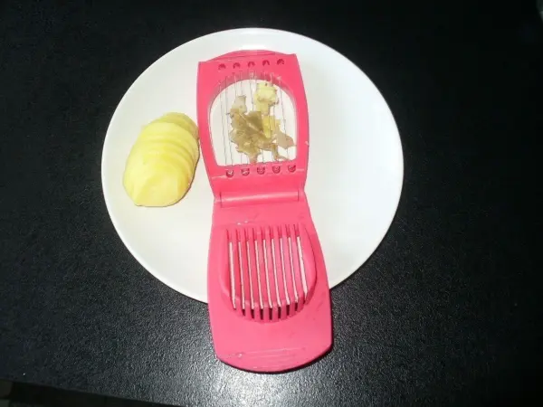 Pellkartoffeln liegen neben einem pinken Schneider, der zum gleichzeitigen Schneiden und Schälen verwendet wird.