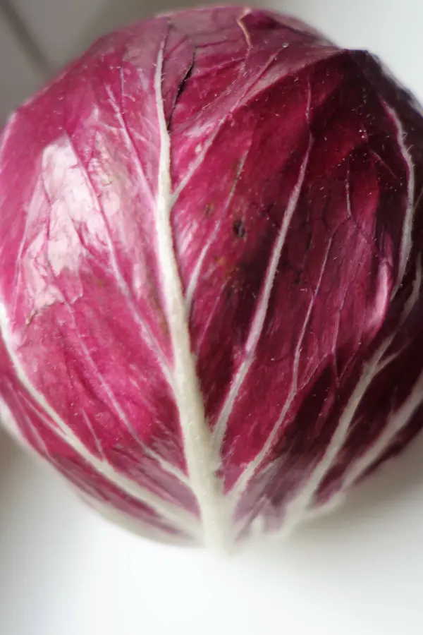 Ein Radicchio-Kopf liegt auf einer hellen Oberfläche, bereit zur Verwendung für Rosen-Stempel. Die Blätter sind tiefrot mit markanten weißen Adern.