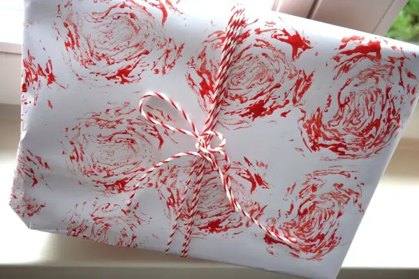 Ein kreativ bedrucktes Papier zeigt rote Radicchio-Rosenstempel in einem dekorativen Muster, liebevoll mit einer Schnur gebunden.