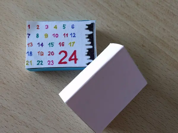 Ein kleines Streichholzschachtel-Set liegt auf einem Tisch, das den Adventskalender mit dem 24. Tag zeigt.