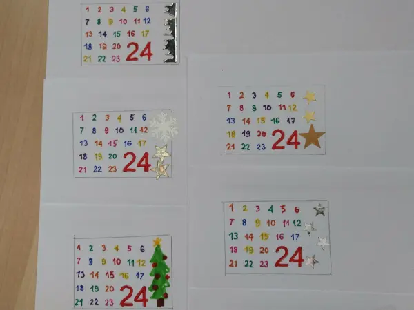 Bunte Adventskalenderkarten zeigen das Datum 24, umgeben von festlichem Zubehör auf einem Tisch.