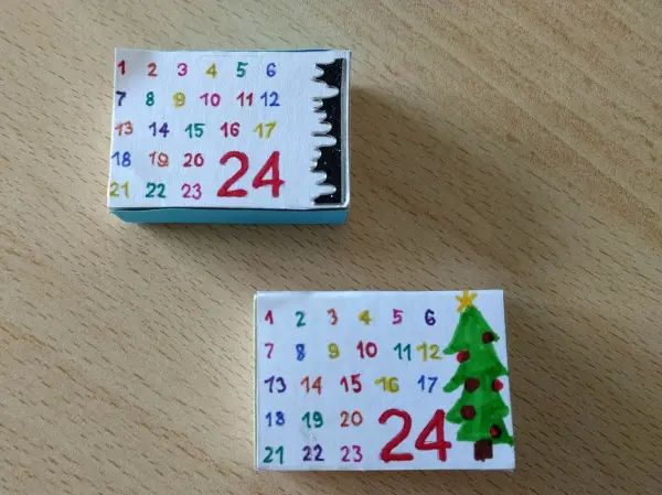 Zwei kleine Streichhölzer zeigen Mini-Adventskalender mit den Zahlen 1 bis 24 und einer Dekoration für Weihnachten.