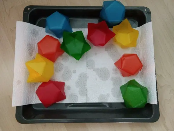 Bunte, geometrische Formen liegen auf einem Tablett auf Küchentuch, bereit zum Basteln für Papier-Windlichter im Advent.