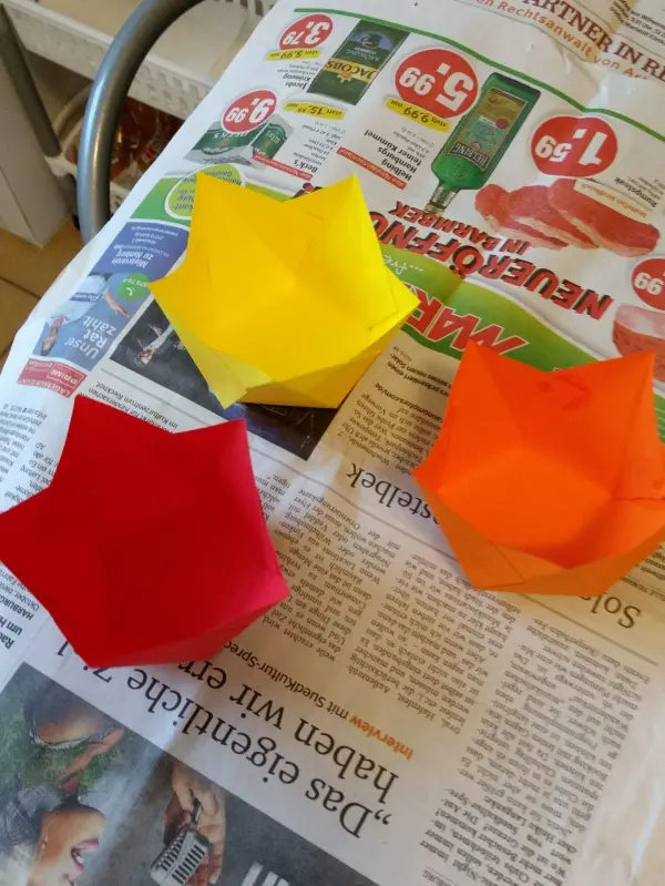 Bunte Papier-Windlichter in Form von Sternen liegen auf einer Zeitung, bereit für eine kreative Bastelaktion im Advent.