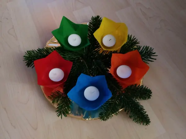 Bunte Papier-Windlichter stehen auf einem Goldteller, umgeben von Tannenzweigen, und verbreiten adventliche Stimmung.