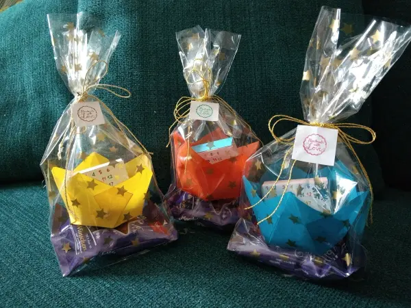 Bunte Papier-Windlichter sind hübsch in Tüten verpackt, umgeben von lila Dekoschnee auf einem grünen Hintergrund.