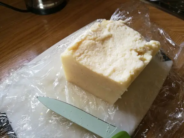 Ein blockförmiger Grießrühm steht auf einer Platte, während ein Messer daneben liegt, bereit zum Schneiden von Grießschnitten.