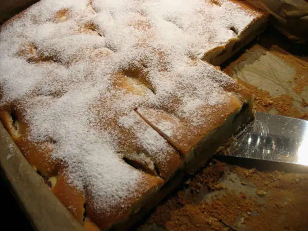 Saftiger Blechkuchen mit weißen Zuckerkristallen wird auf einem Holzbrett geschnitten und serviert.