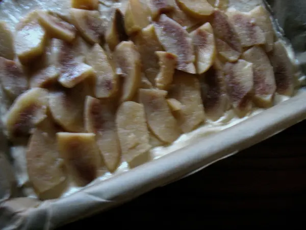 Ein Blechkuchen mit frischen Apfelstücken liegt in einer Backform auf einem Holzuntergrund, bereit zum Backen.