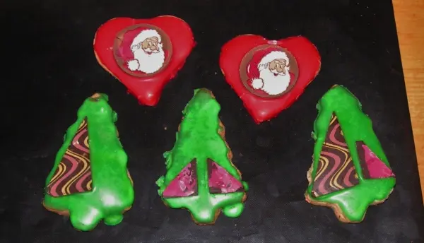 Bunte Weihnachtskekse in Form von Herzen und Bäumen liegen auf einem schwarzen Hintergrund, bereit zum Verzehr.