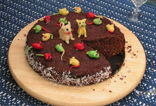 Ein runder Bumerang-Schokoladenkuchen mit bunten, dekorativen Figuren und einer Schnittstelle auf einem Holzbrett.