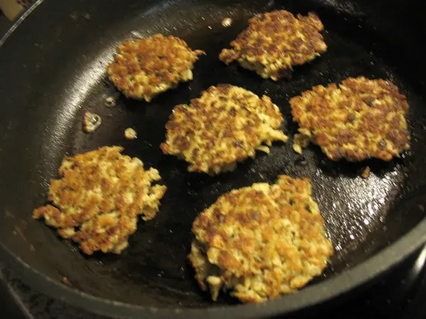 Vegetarische Haferflocken-Puffer bräunen in einer Pfanne, umgeben von heißem Öl in einer einfachen Küche.
