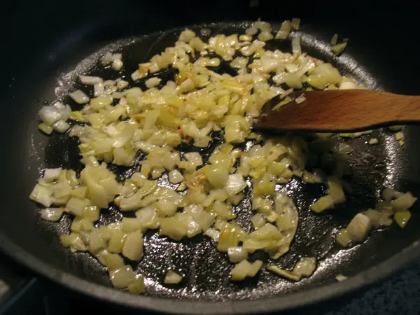 In einer Pfanne braten Zwiebeln goldbraun an, um die Basis für schnelle vegetarische Haferflocken-Puffer zu schaffen.